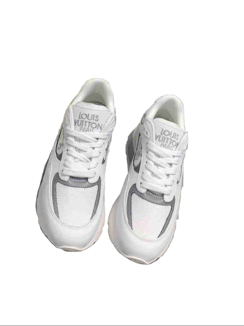 White sneakers with gray accents on a gray surface, next to a colorful Louis Vuitton box.