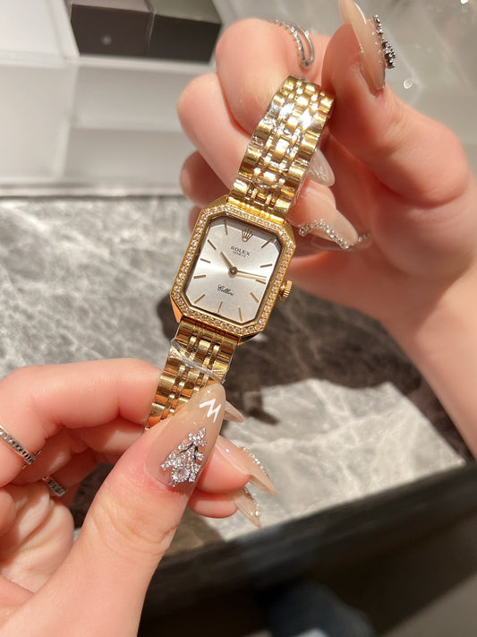 Gold wristwatch held by a hand with decorative nails on a marble surface