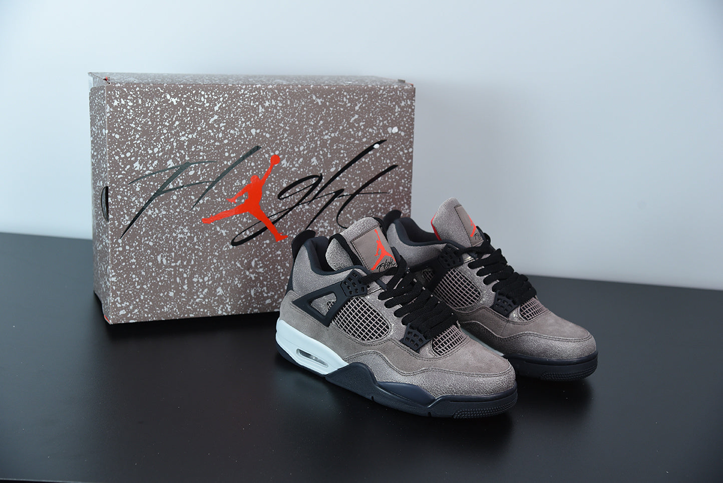 Air Jordan 4 | Taupe Haze | Retro OG Style Gray sneakers with black accents and red logo next to a speckled Jordan box on a dark surface.