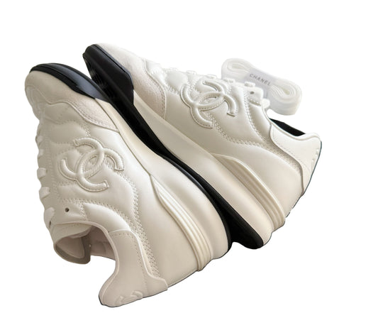 White sneakers with black soles on a Chanel garment with a white background