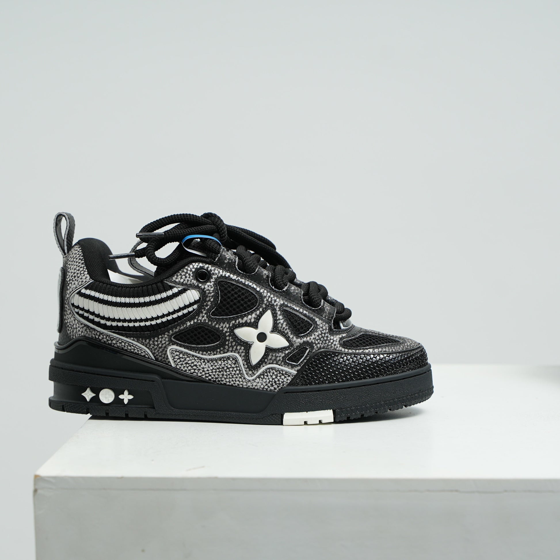 lv Black and gray sneaker with floral design on a white platform against a light gray background