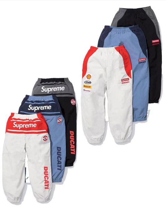 Supreme x Ducati track pants in multiple colorways with Ducati branding, Supreme logos, and racing-style sponsor patches, displayed flat.